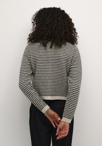 Cropped sweater in light gray knit with dark gray dot pattern. Features long sleeves and a ribbed hem. Soft texture with casual design.