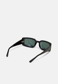 Ochelari de soare dreptunghiulari negri cu lentile verzi, rame din plastic lucios și brațe conice cu un accent logo lângă balama.