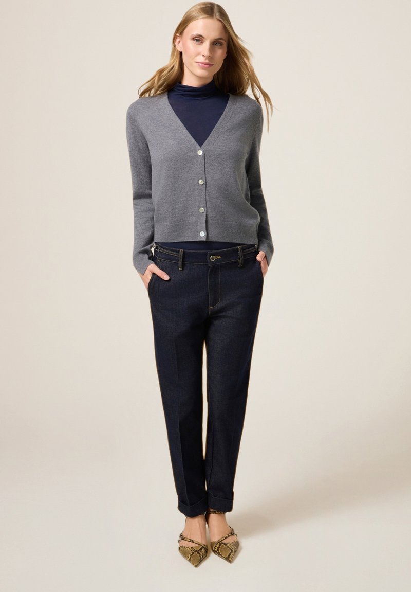 Szary kaszmirowy kardigan z dekoltem w serek i guzikami, noszony na granatowym golfie, w połączeniu z ciemnymi spodniami dżinsowymi i płaskimi butami w wężowy wzór.