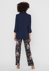 Marinblå blazer med krage och uppvikta ärmar, tillsammans med blommönstrade, vida byxor med rosa och gröna mönster.