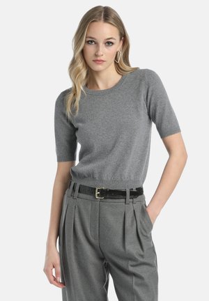 Grauer kurzärmeliger Pullover aus weichem Stoff mit Rundhalsausschnitt. Kombination mit hellgrauen, gefalteten Hosen und einem schwarzen Gürtel.