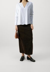 Vit långärmad blus med v-ringning och framsöm, i kombination med en mörkbrun jeanskjol som går till knäna. Svarta loafers och en brun handväska.