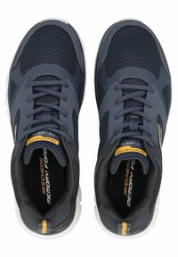 Zapatillas deportivas azul marino con material de malla y sintético, suela de goma blanca, punta redondeada y detalles amarillos en la lengüeta y el talón.