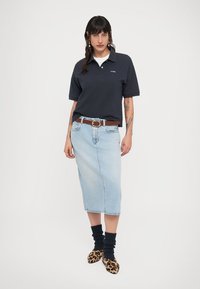 Μπλε μπλούζα πόλο του ναυτικού με κοντά μανίκια, φούστα midi από ανοιχτό μπλε τζιν, καφέ ζώνη, σκουρόχρωμες κάλτσες με υφή και παπούτσια με σχέδιο λεοπάρ.