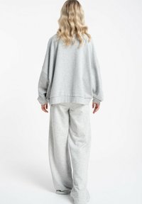 Szara bluza o luźnym kroju i obniżonych ramionach, w komplecie z szerokimi, szarymi spodniami dresowymi. Miękki, teksturowany materiał o swobodnym wyglądzie.