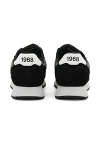 Un paio di sneaker bianche e nere viste dal retro, ciascuna con "1968" stampato sulla linguetta bianca del tallone.