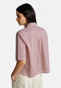 Chemise à manches courtes en tissu léger avec un motif géométrique en violet et rose. Col en V et coupe décontractée, ample.