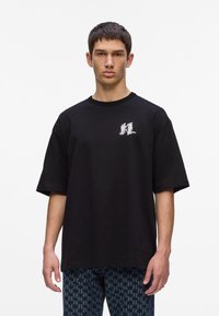 Zwart oversized t-shirt van katoen met een ronde hals en korte mouwen. Bevat een wit grafisch logo op de linkerkant van de borst.