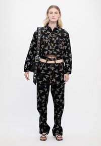 Black cropped jacket and matching pants with a graphic print. Features include a cropped design, belt accents, and a large strap.