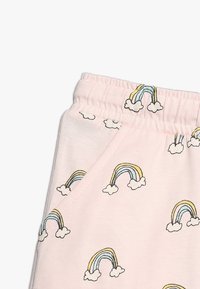 Jasnoróżowe bawełniane spodnie z wzorem kolorowych tęczy i chmur, z elastycznym pasem i detalem kieszeni bocznych.