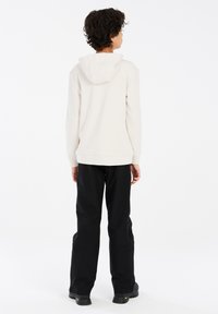 Felpa beige con cappuccio, polsini e orlo a coste. Abbinata a pantaloni neri larghi e calzature nere robuste, vista da dietro.