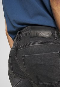 Jeans de mezclilla negra con un acabado texturizado, que presentan una etiqueta de cuero de la marca LTB en la parte trasera de la cintura y bolsillos traseros visibles.