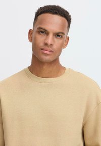Beige crewneck sweatshirt made of soft fabric. Features a ribbed neckline and slightly loose fit, with no patterns or graphics.