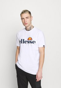 White cotton T-shirt featuring a large blue "ellesse" logo and a colorful half-circle accent above the text. Short sleeves and a round neckline.