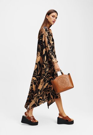 Robe à motif floral noir avec des manches longues, associée à des sandales compensées marron et à un sac à main beige avec des découpes.