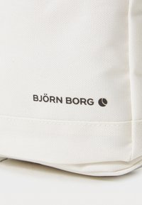 Hvit stoffveske med en teksturert overflate, med en svart "BJÖRN BORG" logo og rund aksent. Konsis, minimalistisk design.