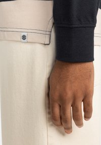 Zwarte langesleeve shirt van textuurstof met lichtbeige accenten, voorzien van zichtbare naden en een klein merkembleem op de zoom.