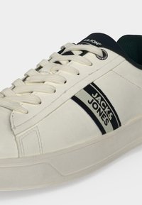 Baskets basses blanches avec lacets blancs, bandes latérales noires et grises, et marquage "Jack & Jones" sur le côté et la languette.
