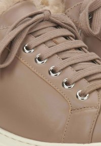 Beige leren sneakers met een gestructureerd oppervlak, voorzien van ronde zilveren oogjes, beige veters en een zachte bontvoering bij de kraag.