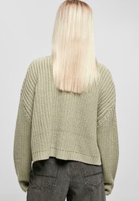 Stickad grön tr�öja med lös passform, vida ärmar och kortad fåll, kombinerad med mörkgrå byxor. Den texturerade designen ökar djupet.