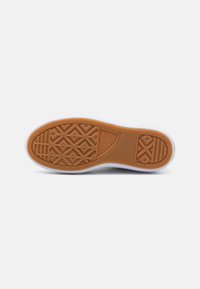 Suela de zapato de goma con un patrón texturizado de panal en marrón. Bisel blanco alrededor de la suela y una marca que presenta "Converse" y "All Star."