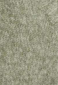 Primo piano di un tessuto lavorato a maglia verde chiaro con una texture morbida e pelosa e anelli di filo visibili in un motivo compatto.