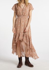 Robe fluide à motifs floraux en beige avec ourlet volanté, manches courtes et taille élastique. Associée à des bottes marron à lacets.