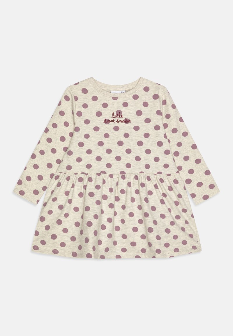 Kopast obleko z dolgimi rokavi v bež bombažu, okrašeno z velikimi burgundskimi pikami in vezenim napisom "mali srčkanec" na prsih. Krožna krila.