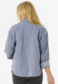 Camicia di velluto a coste blu chiaro con una vestibilità rilassata, texture visibile, maniche arrotolabili e un dettaglio della cucitura del giromanica posteriore.