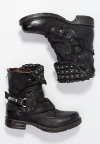 Botines de cuero negro con un acabado texturizado, que cuentan con tachuelas metálicas, una correa con hebilla y un diseño de suela resistente.