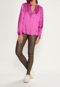 Blouse en satin fuchsia à manches longues et col en V, associée à des leggings marron ajustés et des baskets blanches. Texture lisse et coupe ajustée.