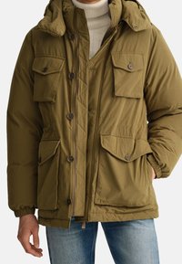 Olivengrøn dynejakke med quiltet tekstur, flere klaplommer, lynlåslukning og justerbar hætte.