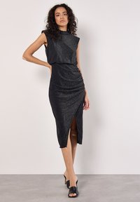 Vestido negro sin mangas en un material brillante con un escote alto, detalles fruncidos y una abertura lateral a la altura del muslo.
