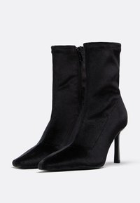 Czarne botki sięgające kostki, wykonane z gładkiego materiału, z ostrym noskiem i szpilkowym obcasem, z boku zapinane na zamek.
