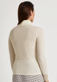 Lichtbeige langetermijn top met ribbeltextuur en hoge kraag. Bevat kantaccenten bij de manchetten en een glad ontwerp van het lichaam.