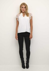 Blouse blanche à manches courtes avec des accents en dentelle sur les épaules, présentant un décolleté en V et une coupe décontractée. Assortie avec un jean skinny noir et des bottines.