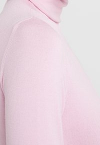 Weicher rosa Rollkragenpullover aus feinem Strickstoff. Er zeichnet sich durch ein figurbetontes Design mit glatter Textur und minimalen Nähten aus.