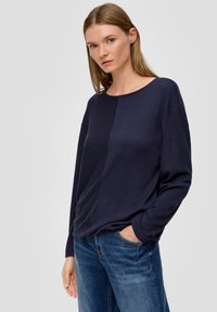 Marineblaues Langarmshirt mit gerippter Textur und Rundhalsausschnitt, kombiniert mit blauen Jeans. Das Shirt hat eine schlichte, lässige Passform.