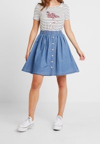 Denim A-linjainen hame, jossa on levenevä muoto, napit edessä, yhdistettynä raidalliseen t-paitaan, jossa on vaaleanpunainen flamingokuvio.