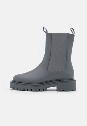 Botte Chelsea gris foncé mi-mollet avec panneaux latéraux élastiques, languettes en haut et semelle épaisse à crampons pour l'adhérence.