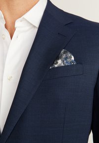 Marinblå blazer med texturerad tyg, slagkrage och en vit skjorta. Fickfåret har ett blått och vitt paisleymönster.