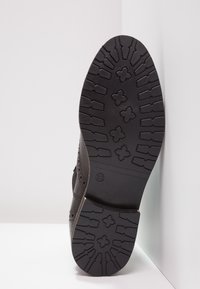 Zapato de cuero negro con una suela texturizada que presenta un dibujo de la banda de rodadura y un marcador de tamaño (37) en el costado.