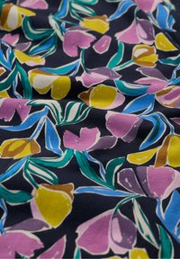 Tkanina w kwiaty o granatowym tle z kolorowymi wzorami fioletowych, żółtych i zielonych kwiatów oraz liści, drukowana w gładkiej, miękkiej teksturze.