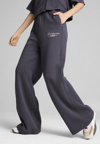 Pantaloni da tuta larghi grigio scuro realizzati in tessuto morbido, con tasche laterali e branding ricamato sul davanti.