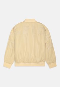 Svetložltá bomber bunda s rebrovaným golierom a manžetami. Obsahuje veľký vyšívaný nápis "TOMMY HILFIGER" na zadnej strane a rukávoch. Hladká textúra.