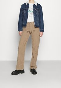 Jeansjacka med fårskinnskrage, vit grafisk t-shirt, beige kordflöjtsbyxor med utsvängda ben och svarta platåstövlar.