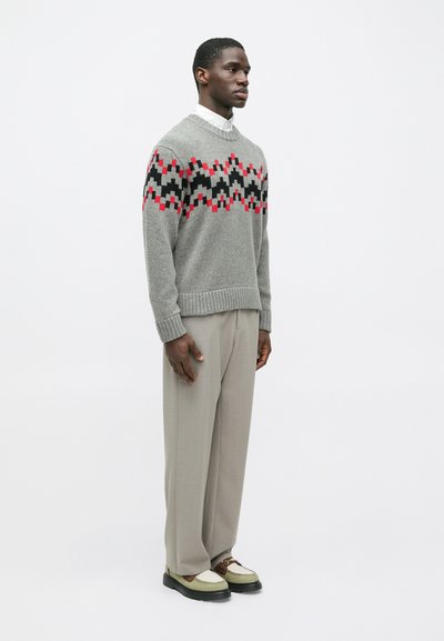 Γκρι πουλόβερ με γεωμετρικό σχέδιο σε κόκκινο, μαύρο και λευκό, συνδυασμένο με μπεζ ψηλόμεσες παντελόνες και μποτάκια πολλών χρωμάτων.