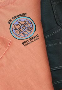 Roze katoenen t-shirt met een rond grafisch ontwerp met zwarte en blauwe letters, gecombineerd met zwarte geribbelde broeken met witte stiksels.