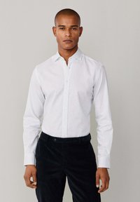 Witte overhemdd met een subtiel stippenpatroon, lange mouwen en een puntige kraag, gecombineerd met donker corduroy broek.