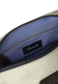 Interno di borsa in tela bianca con rivestimento blu. Presenta una chiusura con zip e un piccolo etichetta nera con il nome del brand, "Façonnable."